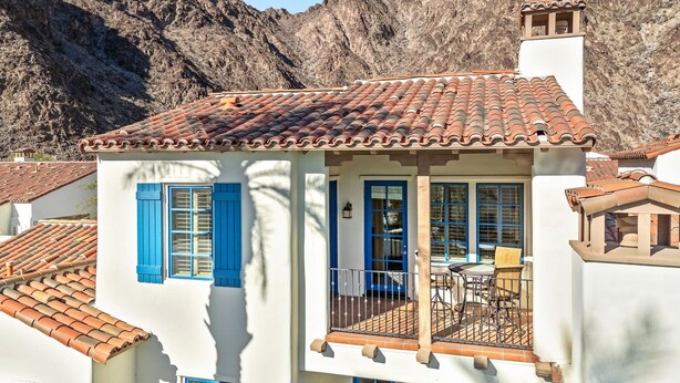 A two-story building with a tiled roof, blue shutters, and a balcony with outdoor furniture. - Luxurious 2 Story Townhome - Newly Remodeled! 3 Bedroom Condo by RedAwning (La Quinta)