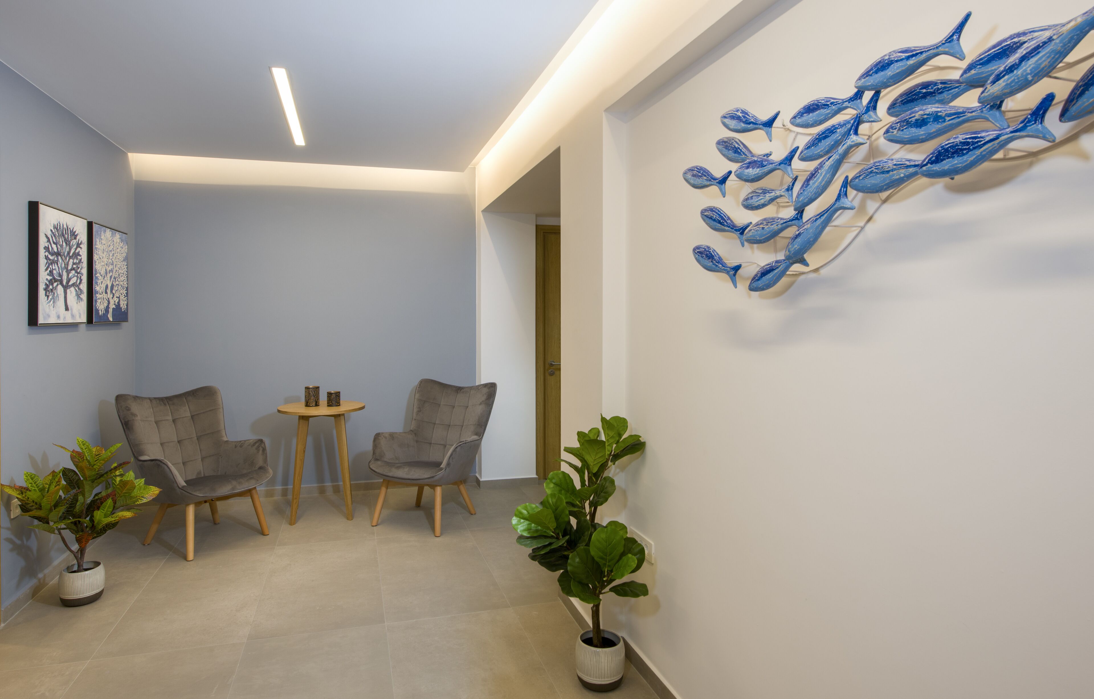 A modern hallway with two grey armchairs, a small round table, and a wall-mounted fish sculpture.