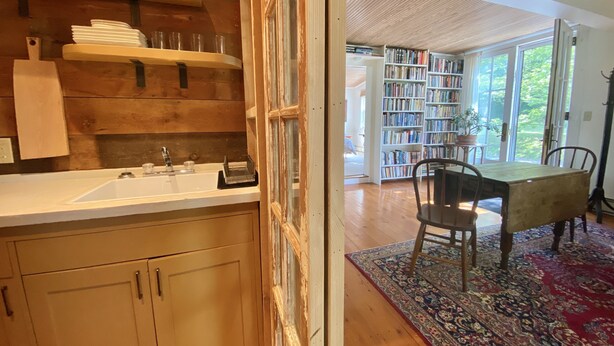 A kitchen with wooden shelves, a sink, and a dining area with a table and chairs. - the suite @ barn & bike - private, bucolic, serene setting (Red Hook)