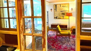 A room with a wooden floor, a yellow chair, a red patterned rug, a bookshelf, and a window with a view of a balcony. - the suite @ barn & bike - private, bucolic, serene setting (Red Hook)