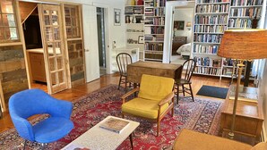 A cozy living room with a blue armchair, a mustard-colored armchair, a coffee table with books, and a bookshelf filled with books. - the suite @ barn & bike - private, bucolic, serene setting (Red Hook)