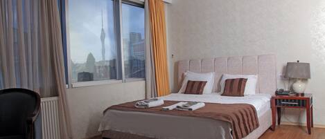 A hotel room with a large bed, a chair, a bedside table with a lamp, and a window with curtains.