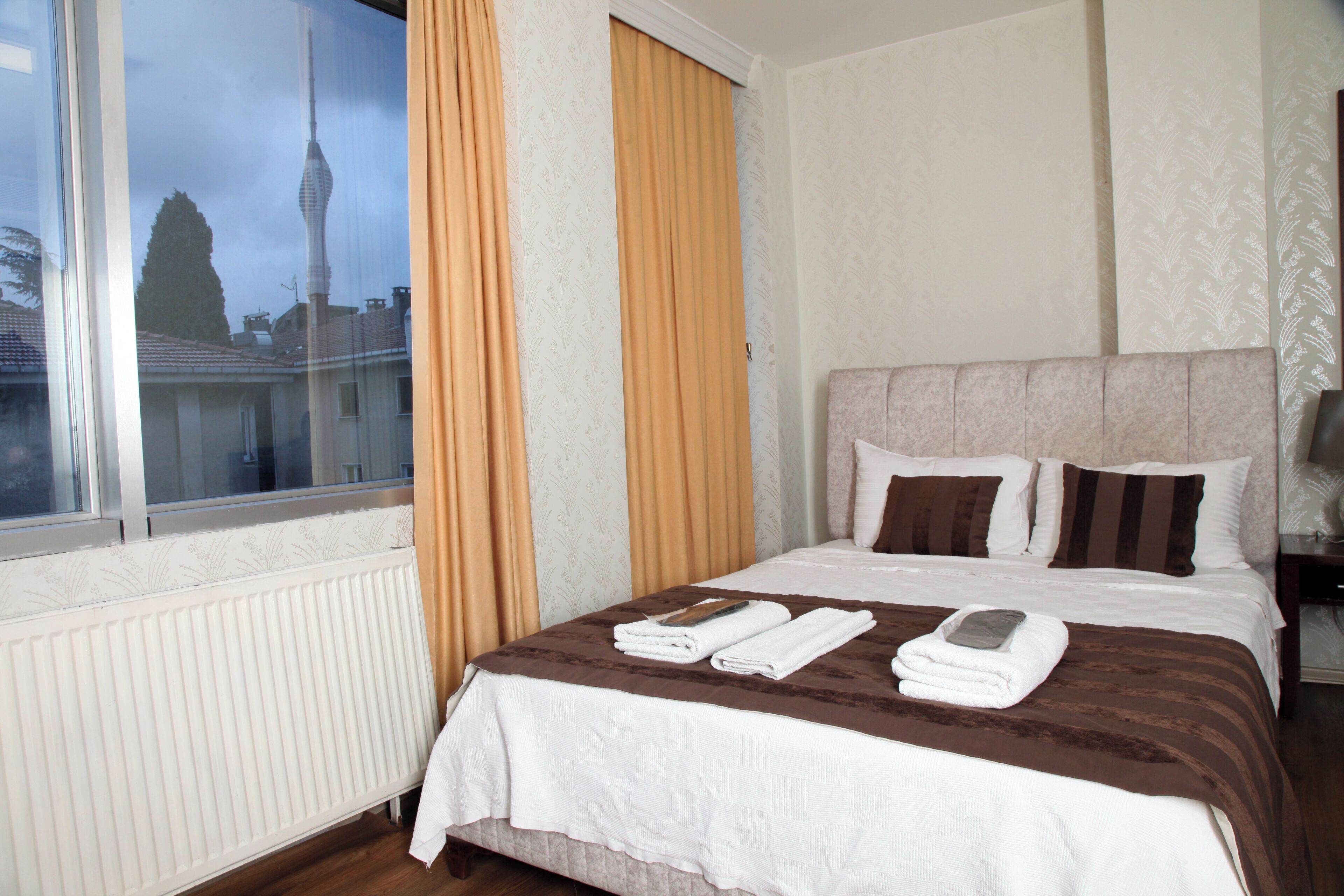 Habitación de hotel con una cama grande, una ventana con cortinas, un radiador y vistas a una torre.
