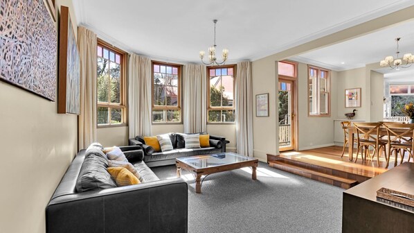 Een ruime woonkamer met een grote zwarte bank, een salontafel, en een eethoek met houten stoelen en een tafel.