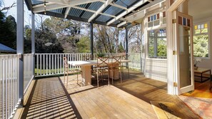 Een overdekt terras buiten, met een tafel en stoelen, omringd door een witte hek en een houten terras.