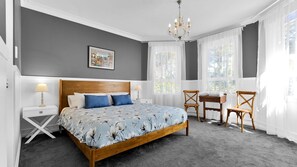 Een slaapkamer met een groot bed, twee nachtkastjes, een kroonluchter, een stoel en een klein tafeltje.