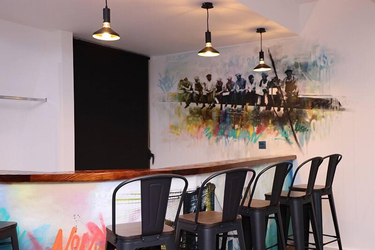 A restaurant interior with a mural, bar stools, pendant lighting, and a wooden counter.