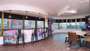 A modern interior with a curved bar area, seating, and large windows offering views of the cityscape. - The Bling Hotel by UStay (Liverpool)