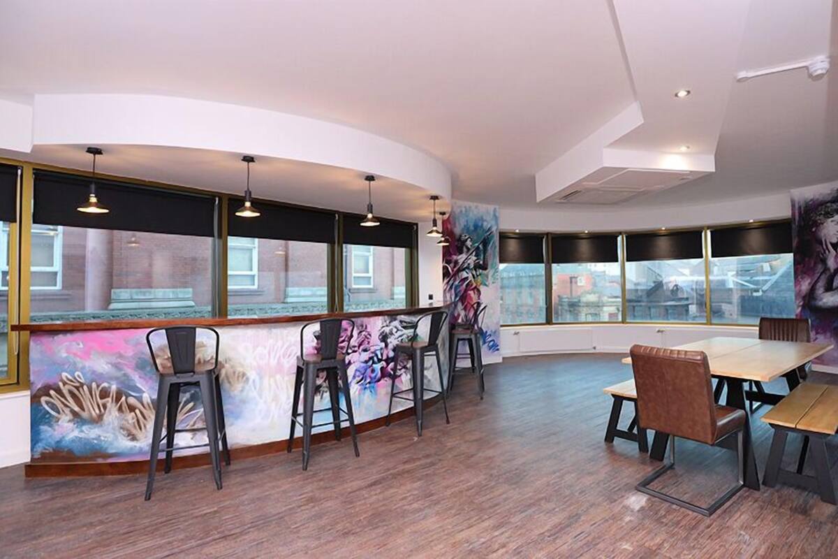 A modern interior with a curved bar area, seating, and large windows offering views of the cityscape.