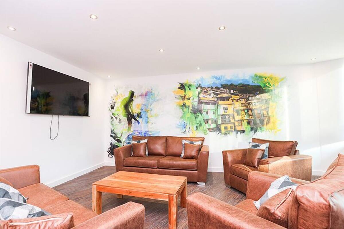 A living room with a brown leather sofa, a wooden coffee table, and a colorful abstract mural on the wall.