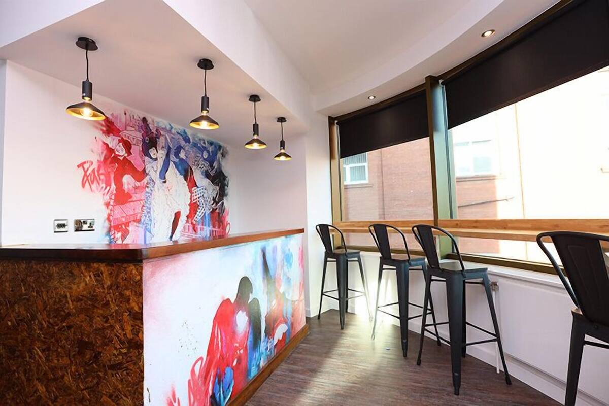 A modern bar area with a wooden counter, black bar stools, and a large window providing natural light.