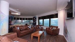 A spacious living area with leather sofas, a wooden coffee table, and large windows offering a view of the cityscape. - The Bling Hotel by UStay (Liverpool)