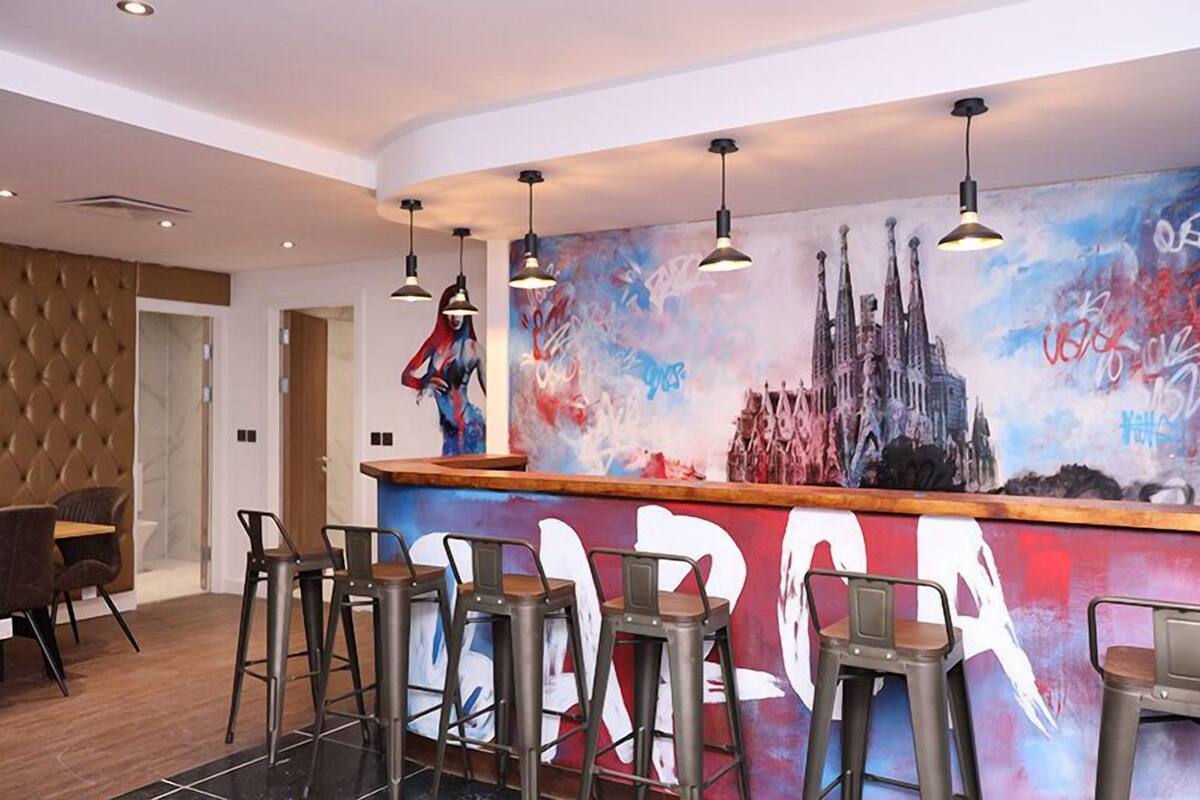 A bar area with a mural of a cityscape and graffiti, bar stools, and pendant lighting.