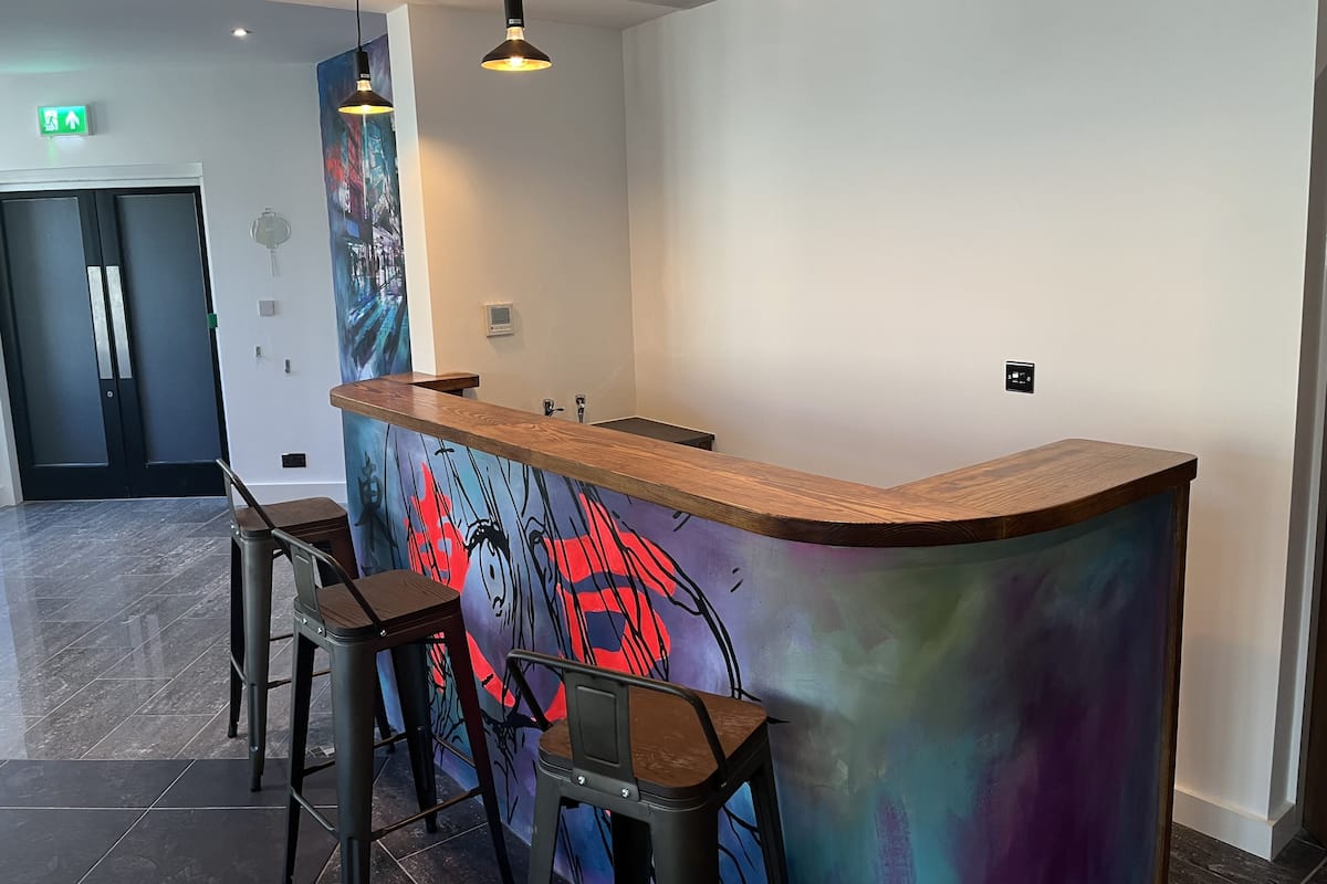 A modern reception area with a wooden counter, bar stools, and a colorful abstract mural.