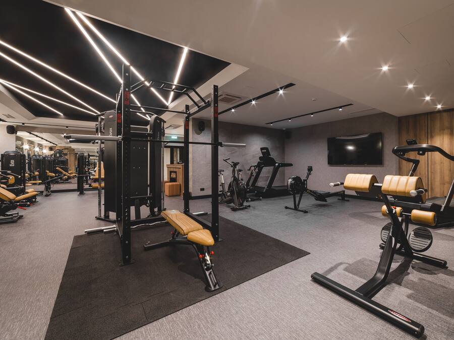 Un gimnasio moderno con diversos equipos de ejercicio, una banca y un televisor en la pared.