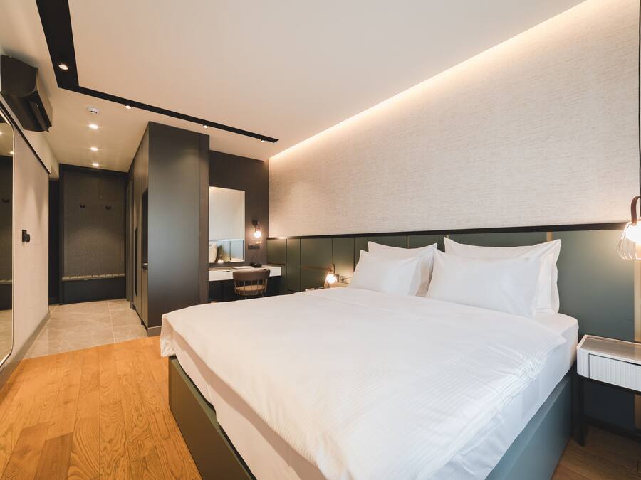 Une chambre d’hôtel moderne avec un grand lit, une table de chevet, un miroir et un téléviseur fixé au mur.