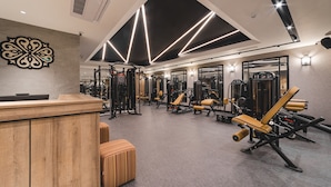 Et fitnessrum med træningsudstyr, en receptionsdisk og et stort spejl.