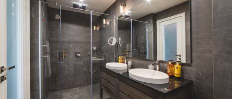 A modern bathroom with two sinks, a glass shower enclosure, and a large mirror.
