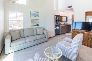 A living room with a sofa, a television, and a dining area with a kitchen in the background.