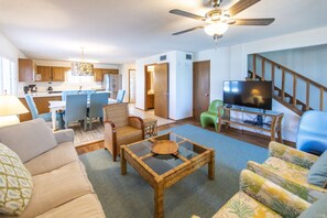 Ein geräumiges Wohnzimmer mit großem Fernseher, Deckenventilator und Essbereich mit Stühlen und Tisch.