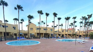 A resort with a pool area, palm trees, and multiple buildings with balconies. - Oasis Royal - Beautiful Corralejo Apartment (Corralejo)