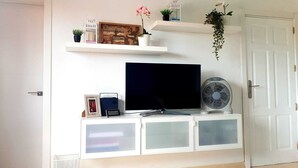 A white entertainment unit with a flat-screen TV, a small clock, and a fan. - Oasis Royal - Beautiful Corralejo Apartment (Corralejo)