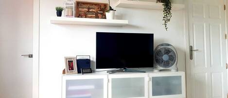 A white entertainment unit with a flat-screen TV, a small clock, and a fan.