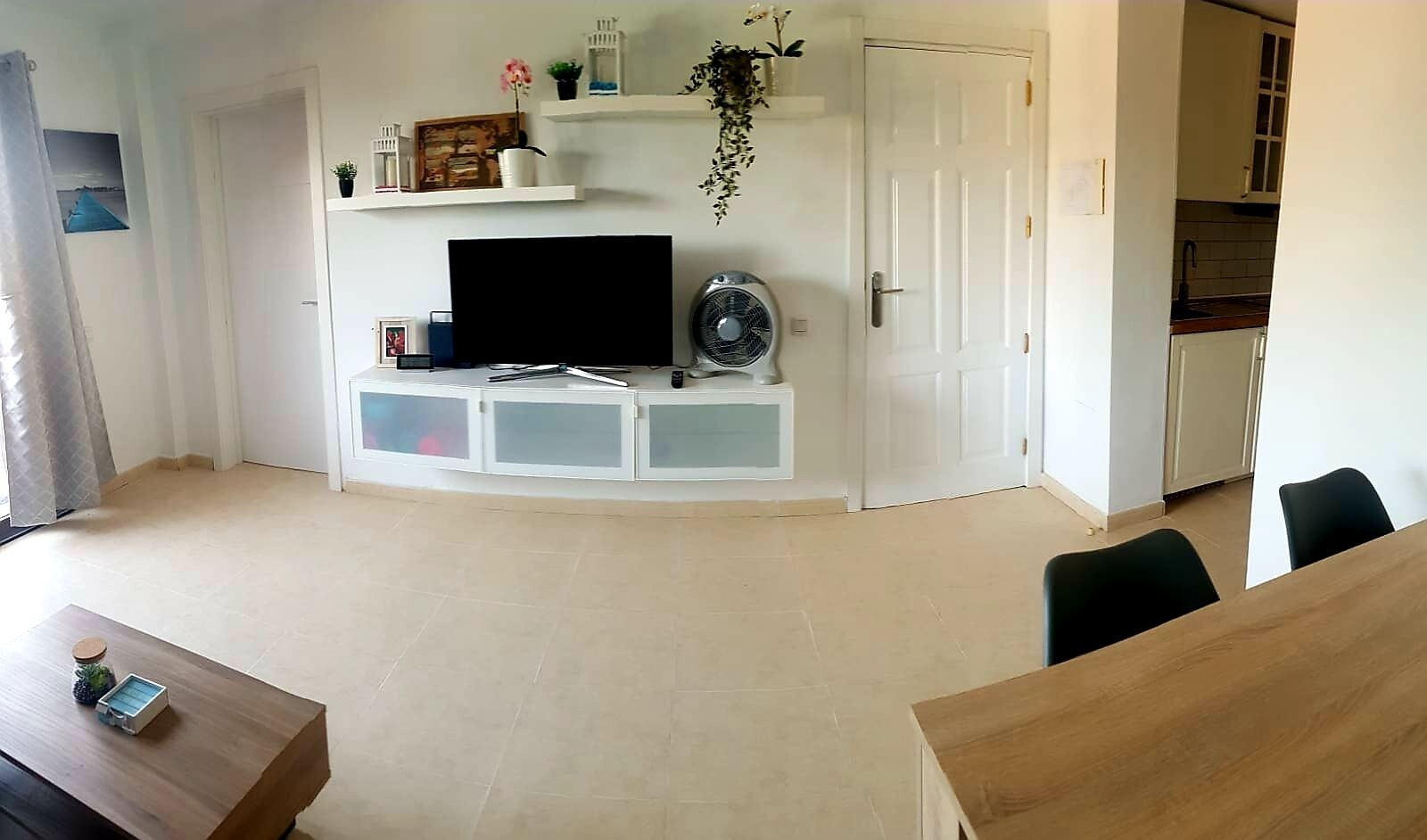 A living room with a TV, white cabinets, a fan, and a dining area with a table and chairs.