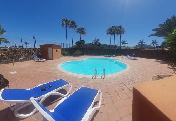 A swimming pool with blue lounge chairs and a stone wall. - Oasis Royal - Beautiful Corralejo Apartment (Corralejo)