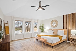 A bedroom with a bed, bedside table, lamp, and a view of trees through large windows.