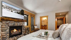 Een knus slaapkamer met een stenen openhaard, een bed met een dienblad, en uitzicht op een besneeerd landschap.