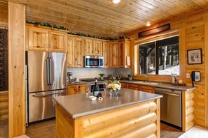A log cabin kitchen with wooden cabinets, stainless steel appliances, a large window, and a wooden island.