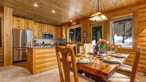 Een houten chalet van binnen met een eethoek, keuken en grote ramen.