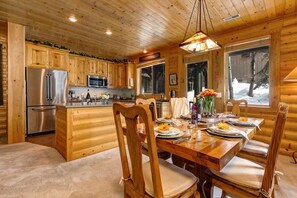 A wooden cabin interior with a dining area, kitchen, and large windows.