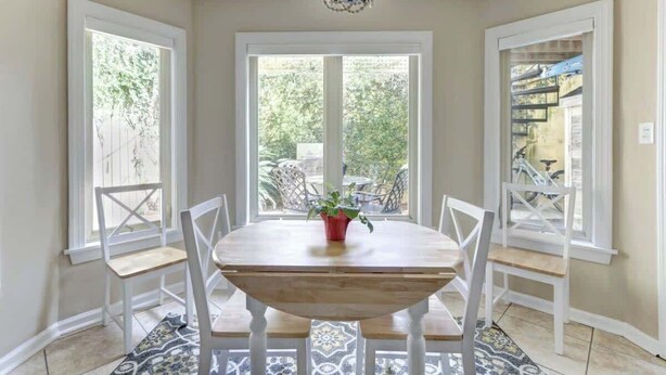 A dining area with a wooden table and white chairs, large windows with a view of greenery, and a decorative ceiling light. - Circa 1870, Historic | Central | Original (Savannah)