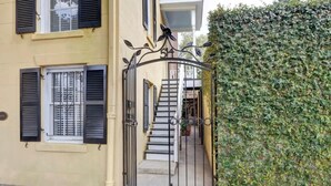 A yellow building with black shutters, a gated entrance, and a staircase leading to an upper floor. - Circa 1870, Historic | Central | Original (Savannah)