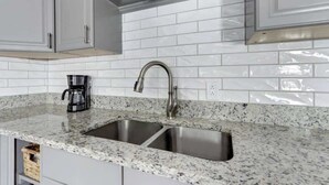 A kitchen with white subway tiles, a granite countertop, stainless steel sink, and a coffee maker. - Circa 1870, Historic | Central | Original (Savannah)