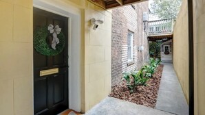 A narrow alleyway with a black door, a green wreath, and a brick building in the background. - Circa 1870, Historic | Central | Original (Savannah)