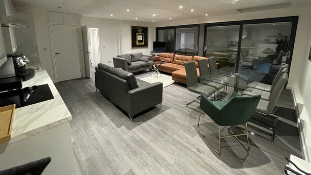 A modern living room with a grey sofa, a brown sofa, and a glass dining table with chairs. - Detached Luxury House in the Hart of Islington (London)
