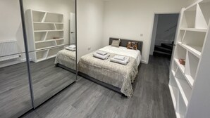 A modern bedroom with a large mirror, a bed with neatly folded towels, and built-in shelving units. - Detached Luxury House in the Hart of Islington (London)