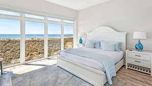 A bedroom with a large window offering a view of the beach, a white bed with blue bedding, and a ceiling fan. - Poseidon's Rest | Gulf Front Home | Gorgeous Gulf Views | Dune Walkover (Navarre Beach)