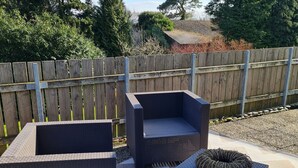 Une terrasse dotée de meubles en osier foncé, notamment d’un canapé et de deux fauteuils, ainsi que d’un pot de fleurs rond en osier.