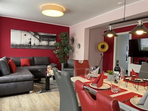 Un soggiorno moderno con un divano grigio, cuscini rossi e un'area pranzo con tavolo apparecchiato per due.