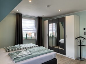 A bedroom with a bed, a wardrobe, a mirror, and a window with curtains. - Fully renovated vacation home—sleeps up to 8, with a sauna and a fenced-in yard (Walkenried)