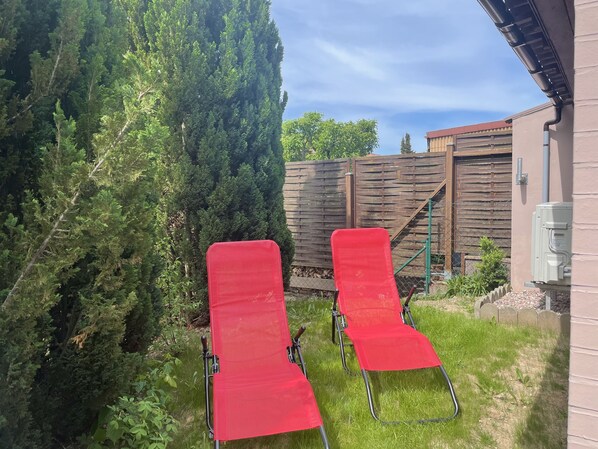 Two red lounge chairs in a grassy backyard with a wooden fence and a tall tree. - Fully renovated vacation home—sleeps up to 8, with a sauna and a fenced-in yard (Walkenried)