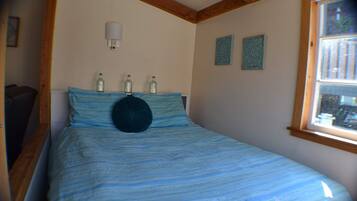 Une chambre à coucher avec un lit, des poutres en bois, une fenêtre et des bouteilles décoratives posées sur la tête de lit.