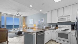 A modern kitchen with white cabinets, a built-in microwave, and an oven. There is a large island with a sink and a dishwasher. The kitchen has a view of the ocean through large windows. - Lighthouse 502 by Liquid Life (Gulf Shores)