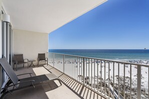 A balcony with two chairs and a table, overlooking a beach with a fence and people. - Lighthouse 502 by Liquid Life (Gulf Shores)