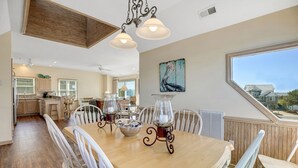 A spacious dining area with a large wooden table, white chairs, and decorative glass pitchers. - Serenity Now: Dog-Friendly Home in Golf Course Community w/ Water Views (Nags Head)
