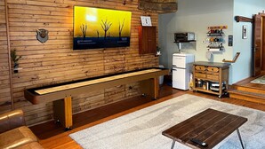 A cozy living room with a wooden wall, a flat-screen TV, a bench, a coffee machine, and a microwave. - The Office at North Creek All Season Rental (North Creek)